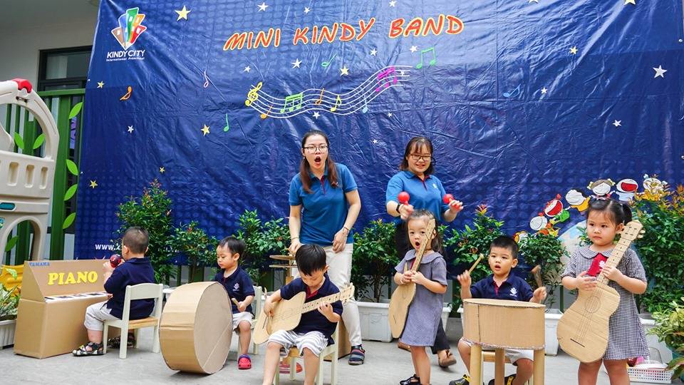 Trẻ đang mải mê biểu diễn nhạc cụ trên nền nhạc có lời trên sân khấu được các cô chuẩn bị sẵn