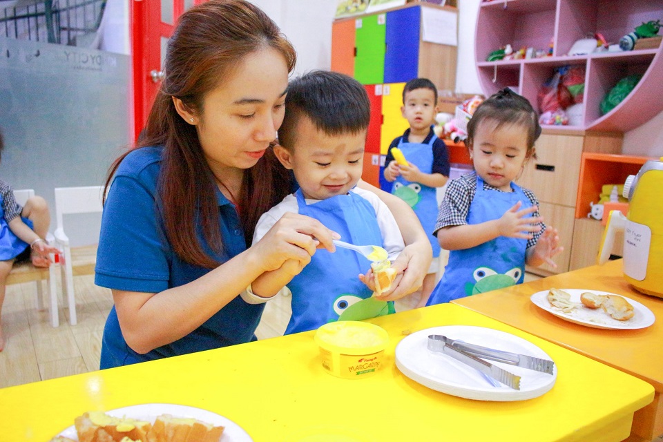 Bé dùng tay phết bơ vào bánh mì, sau đó rắc tỏi và ngò lên trên